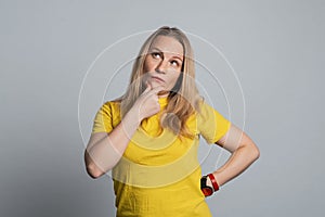 Thoughtful mature woman in casual yellow t shirt is looking up thinking or planning. Concept of doubtful mind