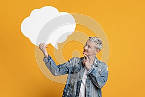 Thoughtful mature woman holding and looking at blank speech bubble with curiosity
