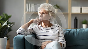 Thoughtful mature woman sitting on couch, dreaming and planning