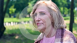 Thoughtful mature woman sitting outdoors, weekend in countryside, tranquility