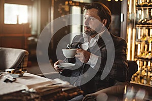Thoughtful mid-aged businessman drinking coffee and looking away in restaurant