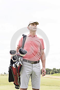 Thoughtful middle-aged man looking away while carrying golf bag against clear sky