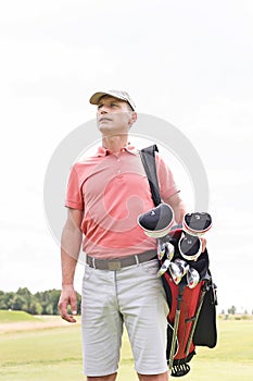 Thoughtful middle-aged man looking away while carrying golf bag against clear sky