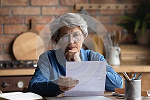 Thoughtful middle aged woman in eyeglasses reading paper letter carefully.