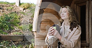 Thoughtful middle aged woman in her forties or fifties outside drinking mug of coffee or cup of tea