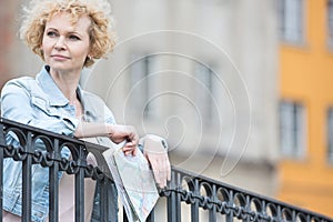 Thoughtful middle-aged woman holding map while leaning on railing