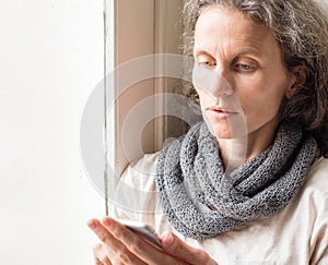 Thoughtful middle aged woman with smart phone