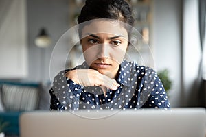 Thoughtful millennial hindu woman looking at laptop monitor.