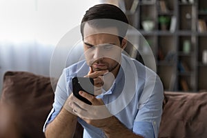 Thoughtful millennial man rubbing chin reading important phone message