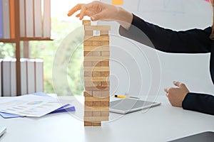 Thoughtful and mindful business woman playing wooden block tower in office. Risk and strategy business concept