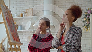 Thoughtful multiethnic teen daughter and mother discussing painting at home