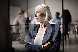 Thoughtful old businesswoman ceo looking through window thinking of leadership