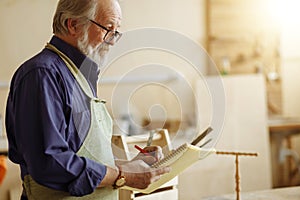 Thoughtful old joiner drawing a sample