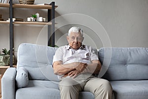 Thoughtful older man sits alone on sofa lost in thoughts photo