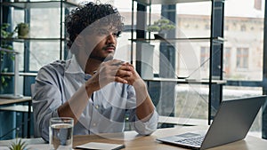 Thoughtful pensive Arabian businessman working with laptop at office desk doubtful Indian Hispanic man looking away