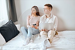 Thoughtful pensive couple sitting on the bed and looking at the window