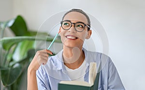 Thoughtful person in glasses hold pencil and book, smiling, contemplation or have idea