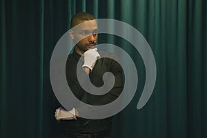 thoughtful portrait of an african american man wearing white gloves. background green curtain drape