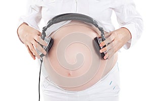 Thoughtful pregnant woman gives an unborn child listen to music using headphones