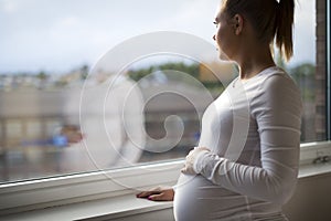 Thoughtful pregnant woman looking out the window