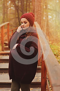 Thoughtful pregnant woman in soft warm cozy marsala outfit walking outdoors