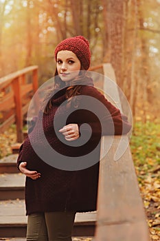 Thoughtful pregnant woman in soft warm cozy marsala outfit walking outdoors
