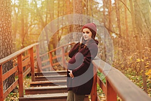 Thoughtful pregnant woman in soft warm cozy marsala outfit walking outdoors