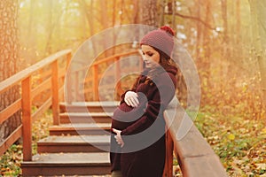 Thoughtful pregnant woman in soft warm cozy marsala outfit walking outdoors