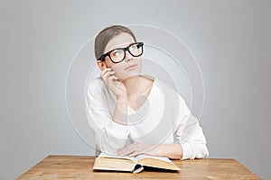 Thoughtful pretty teenage girl in glasses reading book and thinking