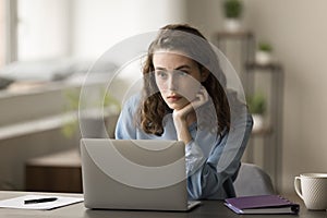 Thoughtful pretty young freelance employee woman working at laptop