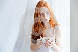 Thoughtful redhead woman holding cup with tea