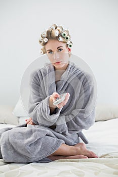 Thoughtful relaxed blonde woman in hair curlers using a remote control