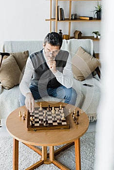 Thoughtful retired man in glasses looking at chess board