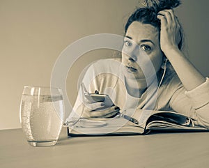 Thoughtful and sad attractive girl with mobile phone and headphones, grey background. On the table glass of water, organizer and