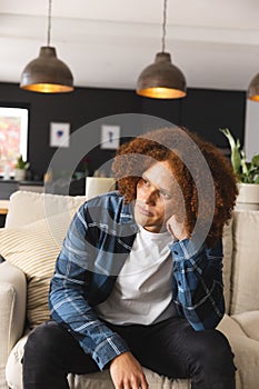 Thoughtful, sad biracial man sitting on couch in living room, looking away, copy space