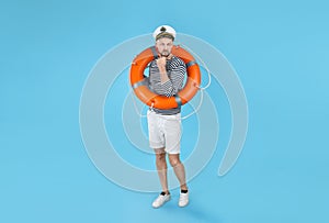 Thoughtful sailor with orange ring buoy on light blue background