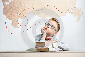 A thoughtful schoolboy sits at a desk with books