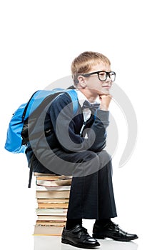 thoughtful schoolboy sitting on a pile of books on a white background