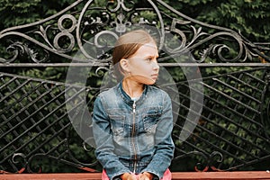 Thoughtful scowl candid eight year old kid girl sits on bench and observe nature. prepubertal age of children and their lives, min