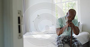 Thoughtful senior african american man in bedroom holding walking cane