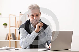 Thoughtful senior businessman looking at laptop at home