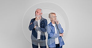 Thoughtful senior husband and wife with hands on chins looking away and standing on white background