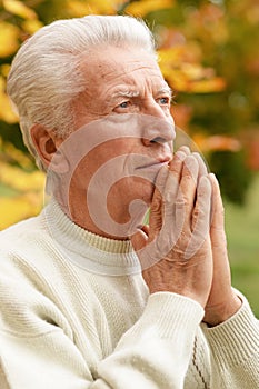 Thoughtful senior man praying in autumn park