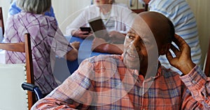 Thoughtful senior man sitting in wheelchair while senior friends interacting in background 4k