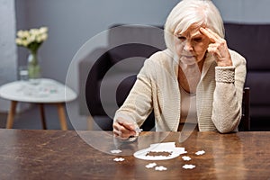 Thoughtful senior woman collecting jigsaw puzzle