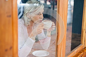 Thoughtful senior woman drinking coffee while sitting by table