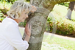 Thoughtful senior woman leaning to tree at park