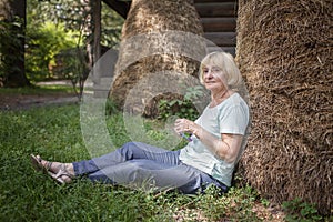 Thoughtful senior woman sits near haystack on farm, plays with fidget sensory toy to relieve stress