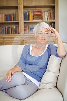 Thoughtful senior woman sitting on sofa in living room
