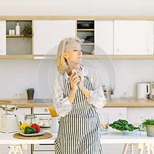 Thoughtful senior woman starting new day with coffee while standing in kitchen at home